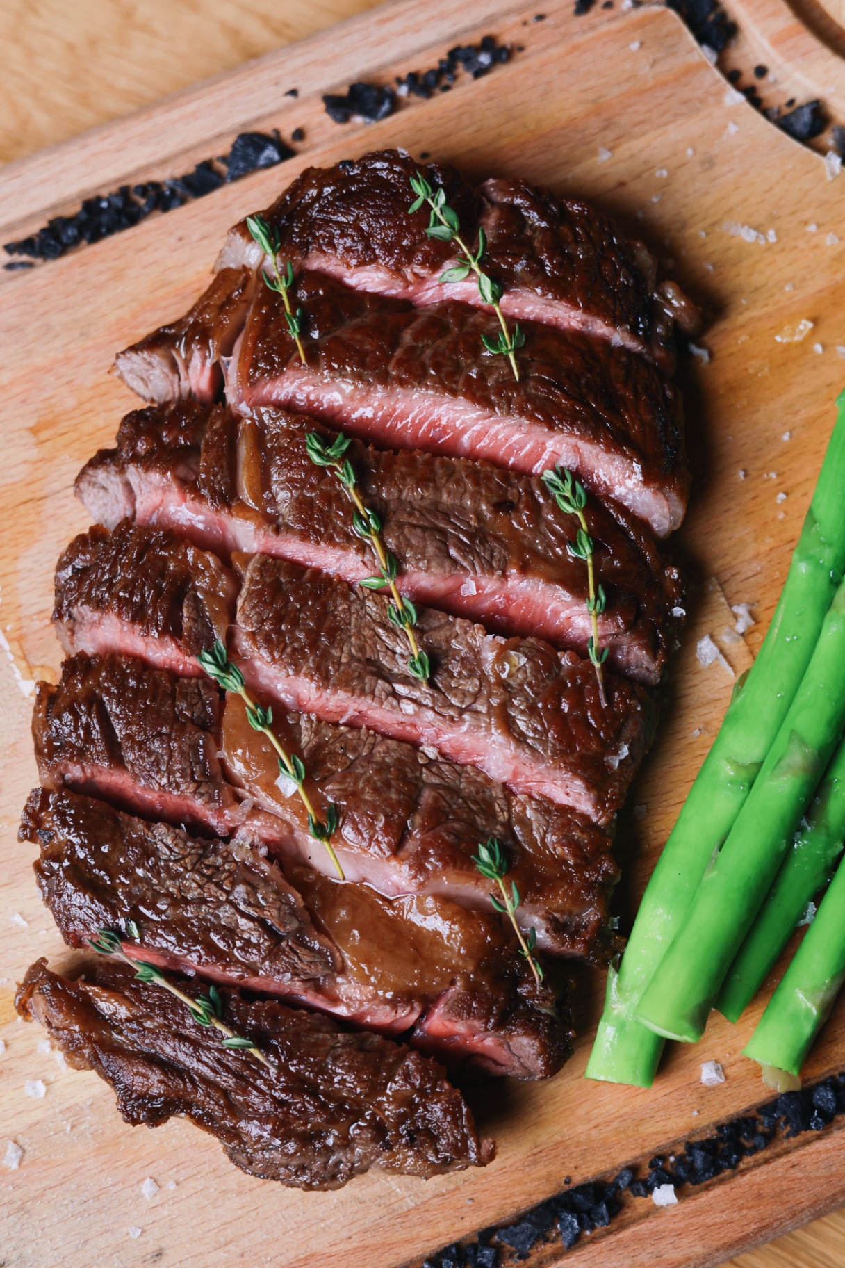 Charcoal-grilled steak with thyme and asparagus on a wooden board at Ujvara